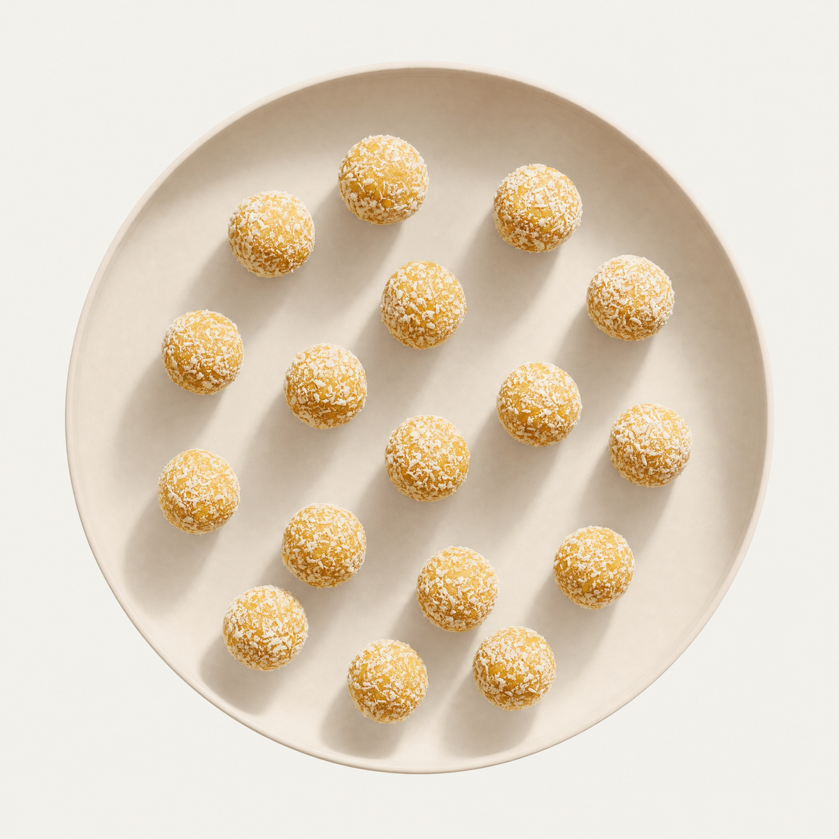 Mango coconut bliss balls on a cream plate, overhead
