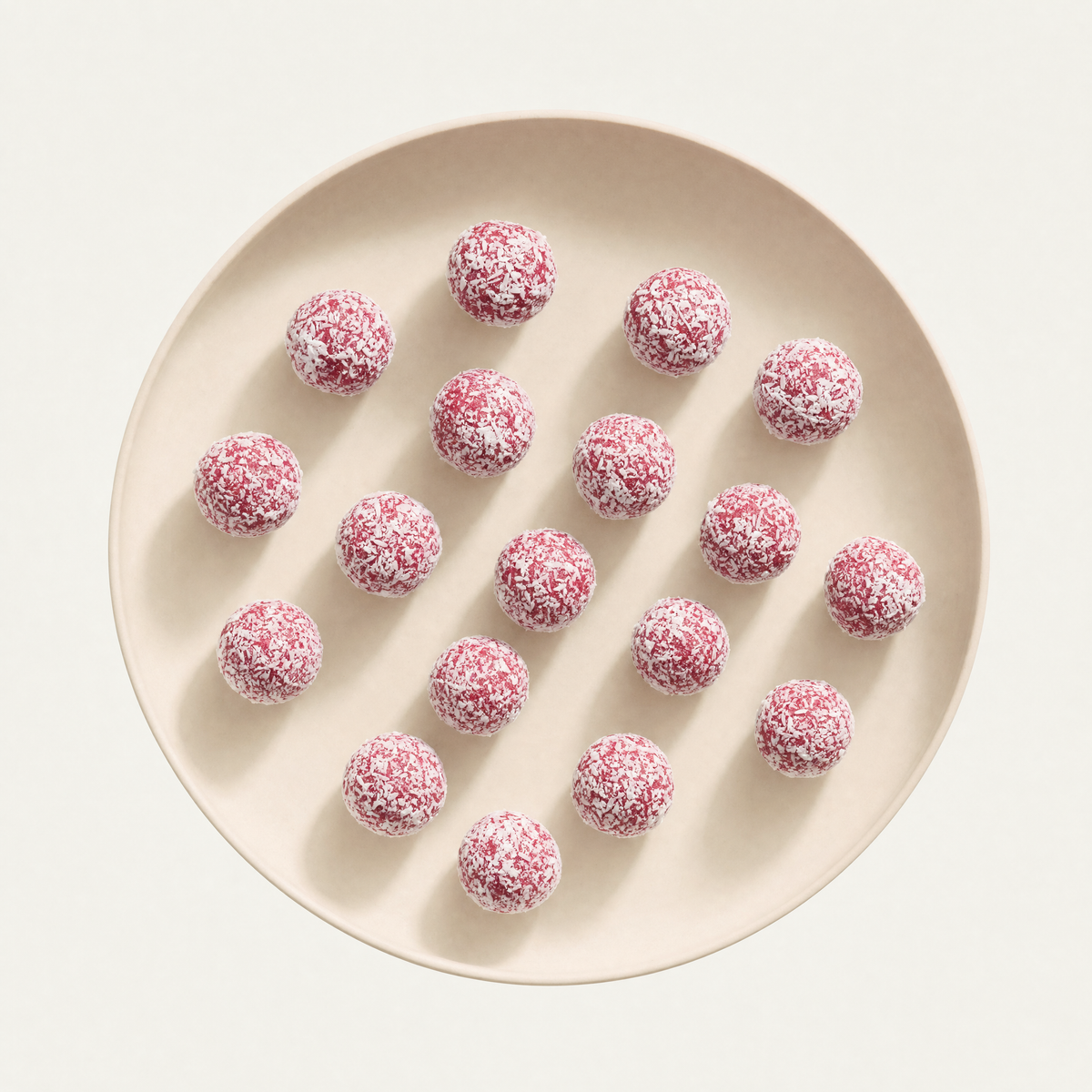 Raspberry coconut bliss balls on a cream plate, overhead